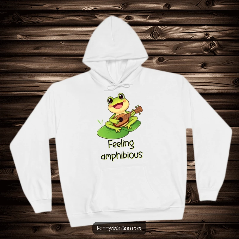 Funny cheerful frog enthusiastically playing a miniature ukulele on a lily pad within a cozy hoodie design.